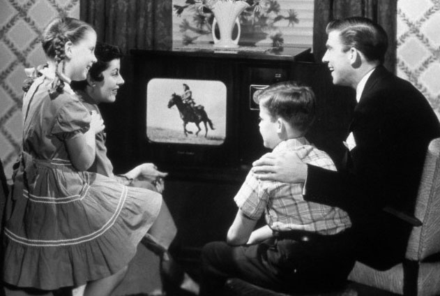 1950s family of four watching black and white television program of a cowboy riding a horse